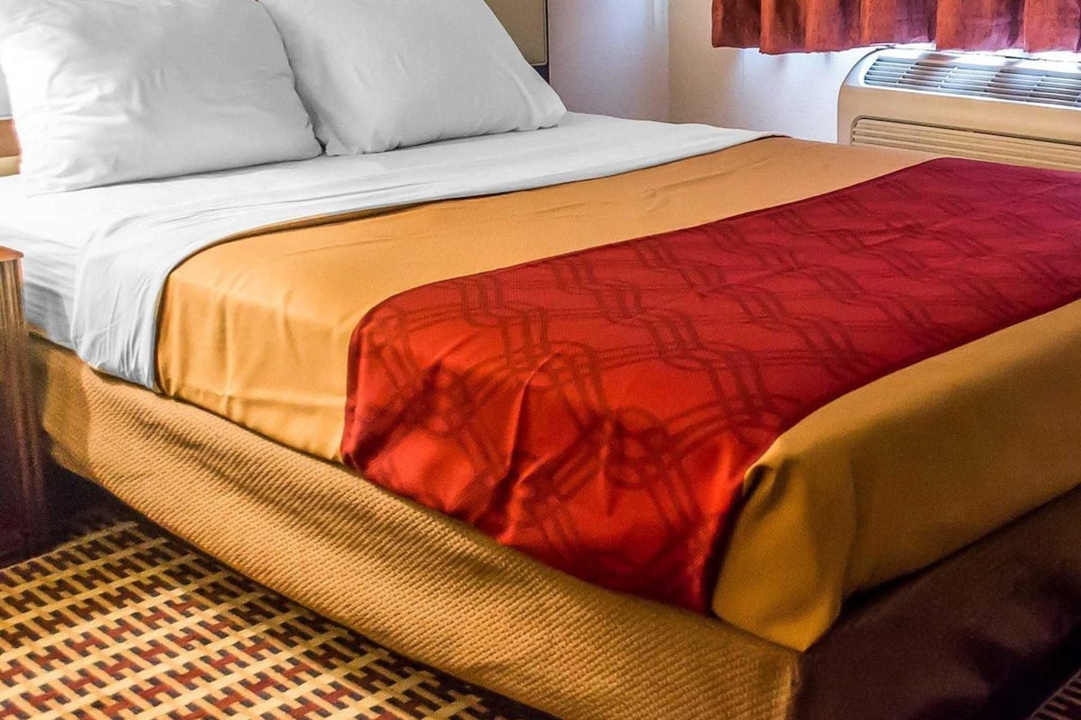 Un lit bien fait, avec une literie blanche et rouge, un couvre-lit à motifs et une tête de lit marron.