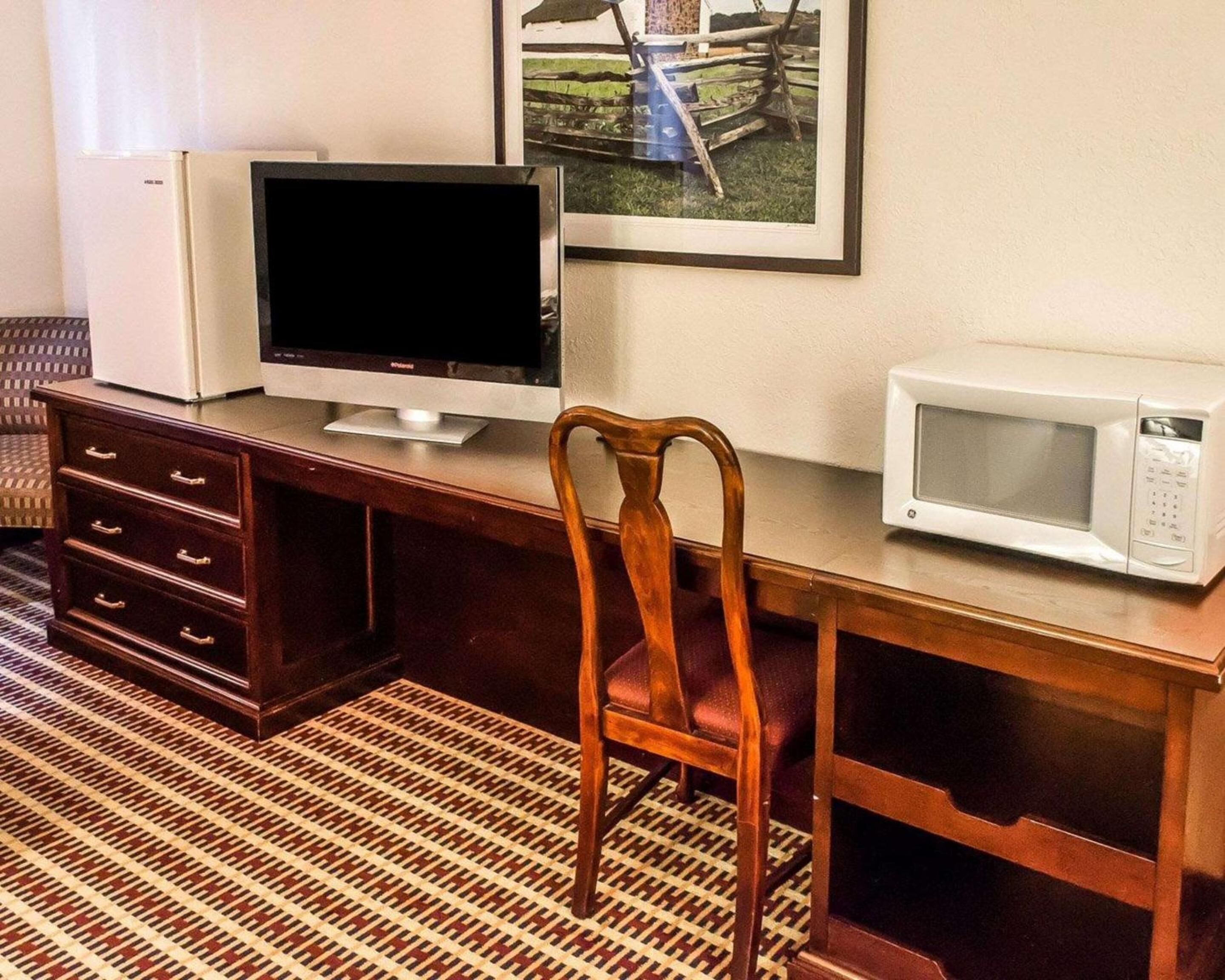 A wooden desk with a television, a microwave, and a chair.