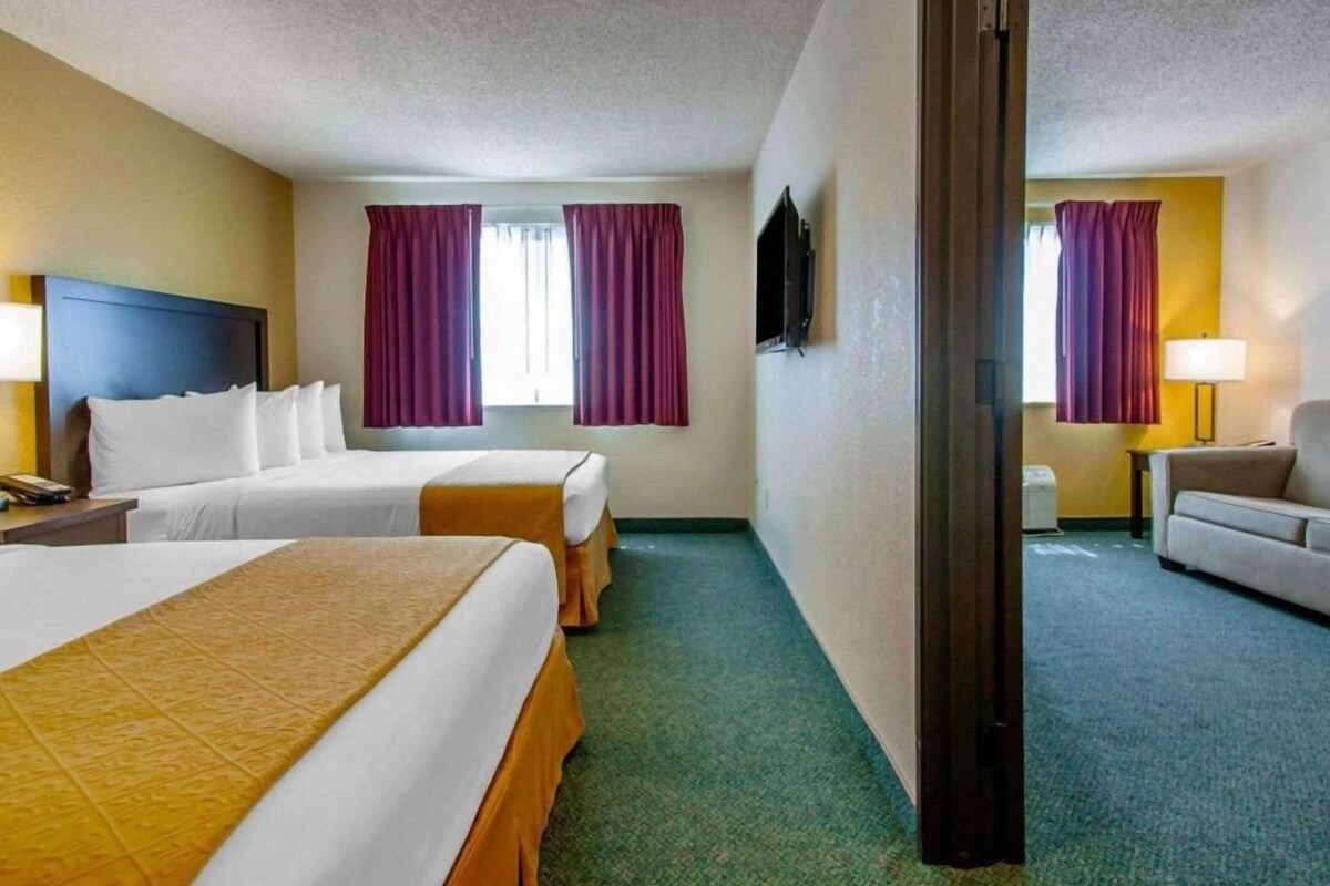 A hotel room with two beds, a sofa, a TV, and a window with curtains.