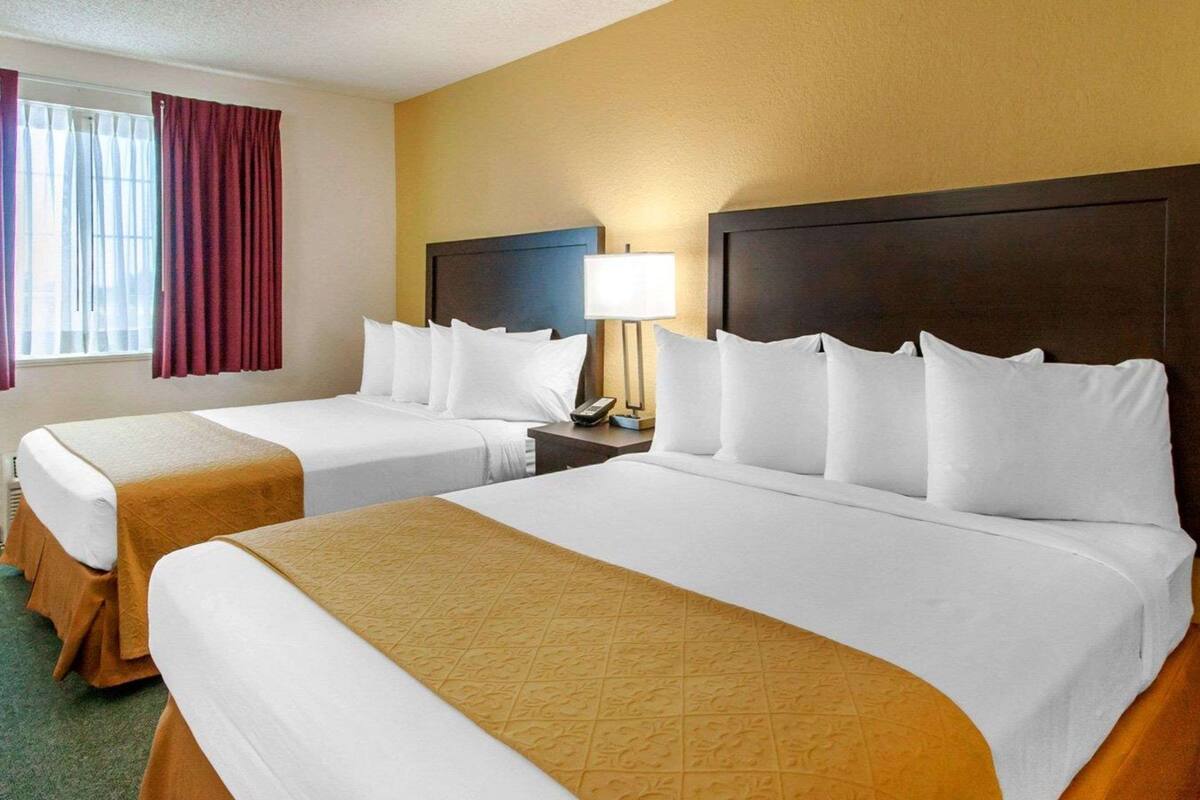 A hotel room with two beds, a nightstand with a lamp, and a window with curtains.