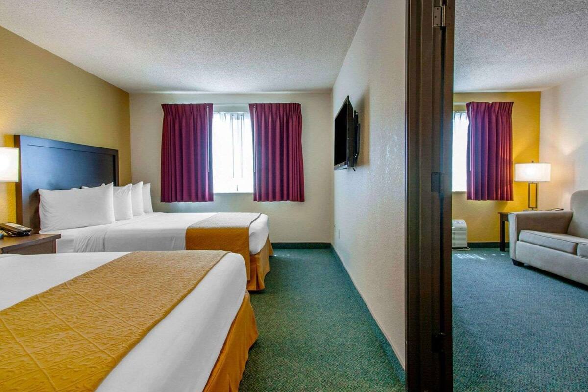 A hotel room with two beds, a desk, a chair, a TV, and a window with curtains.
