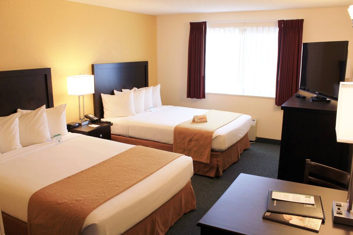 A hotel room with two beds, a desk, a TV, and a window with curtains.
