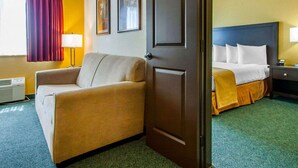 A hotel room with a bed, a sofa, a door, and a window with curtains. - Quality Inn & Suites Springfield - Eugene North (Springfield)