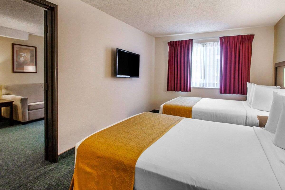 A hotel room with two beds, a television on the wall, and a window with curtains.