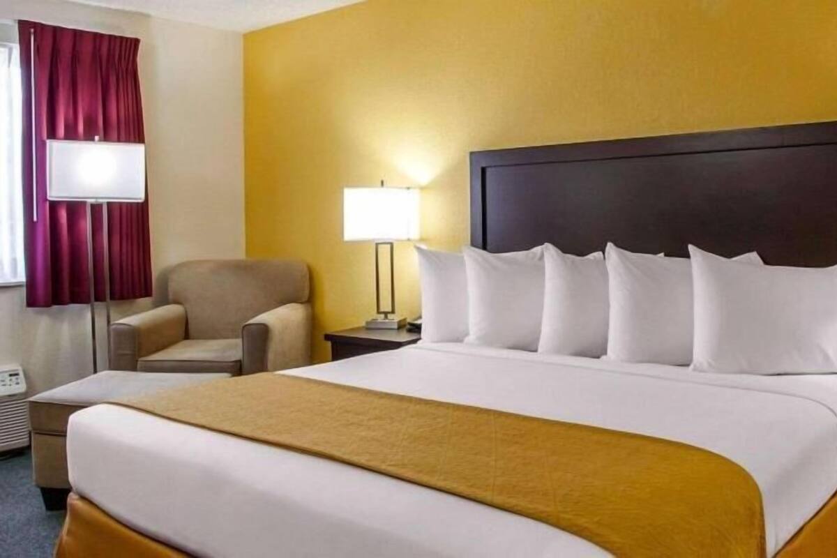 A hotel room with a large bed, a chair, a bedside table, and a lamp.