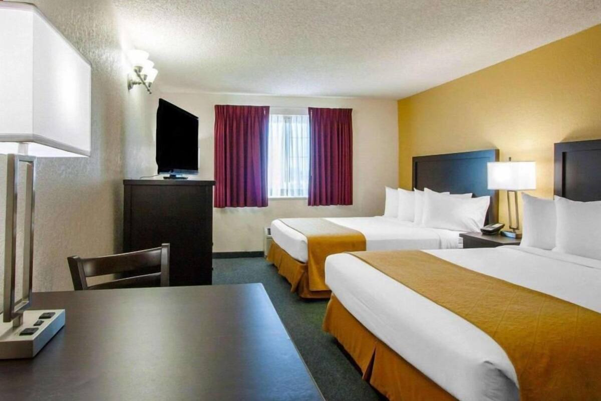 A hotel room with two beds, a desk, a TV, and a window with curtains.