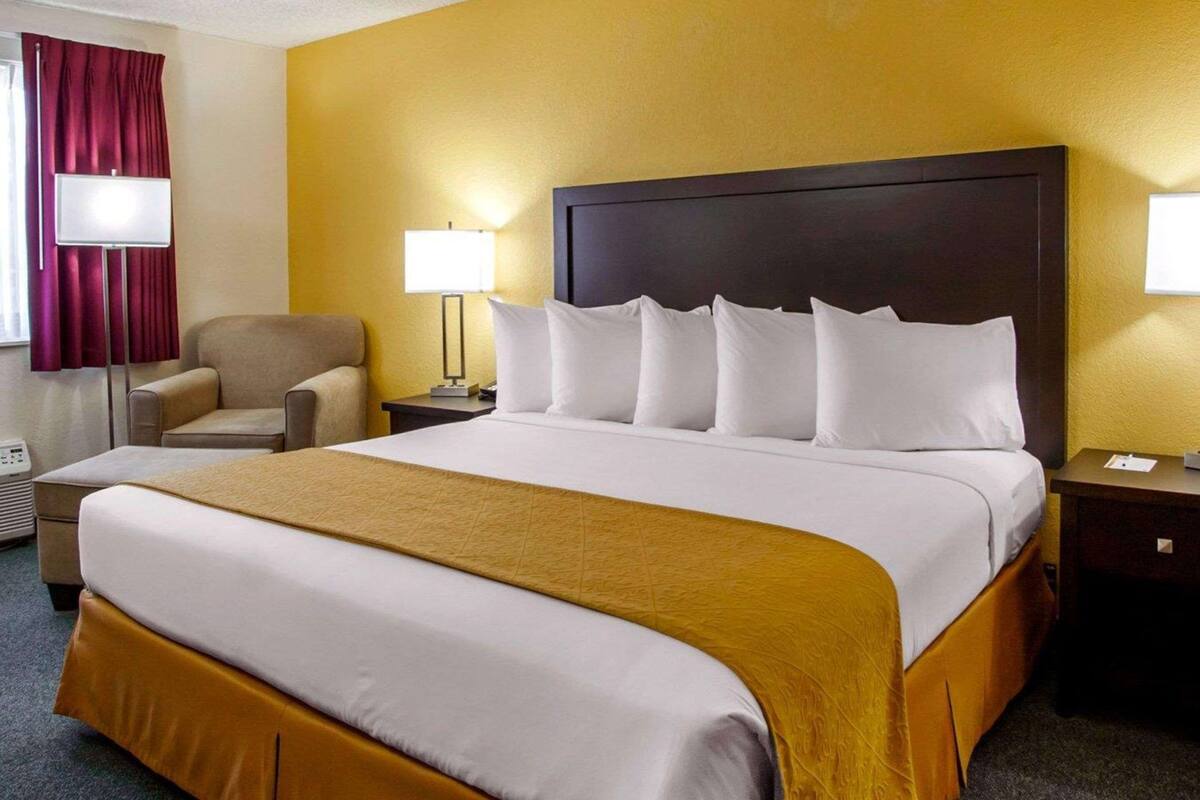 A hotel room with a large bed, a chair, a nightstand with a lamp, and a window with curtains.