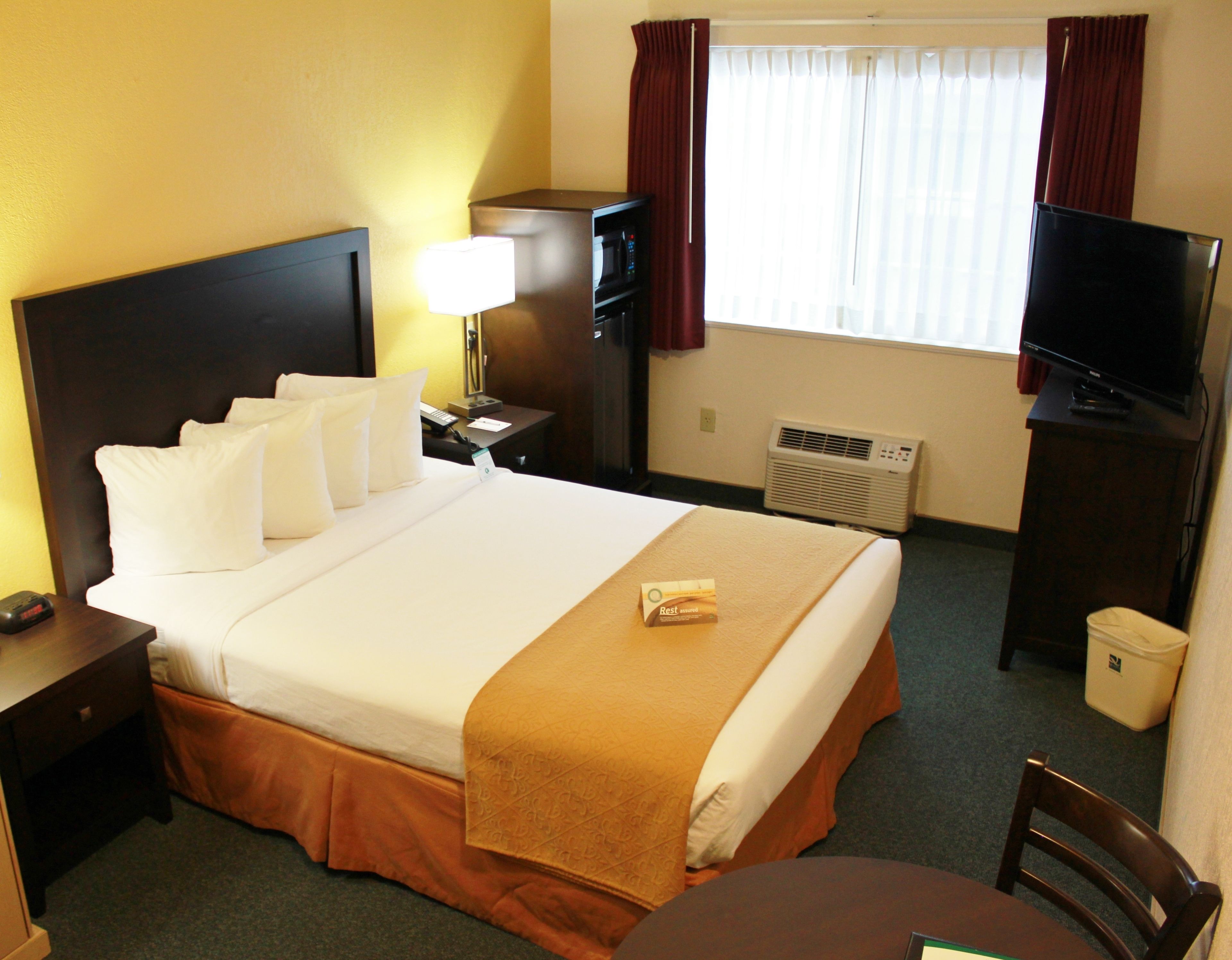 Habitación de hotel con una cama grande, un escritorio, un televisor y una ventana con cortinas.