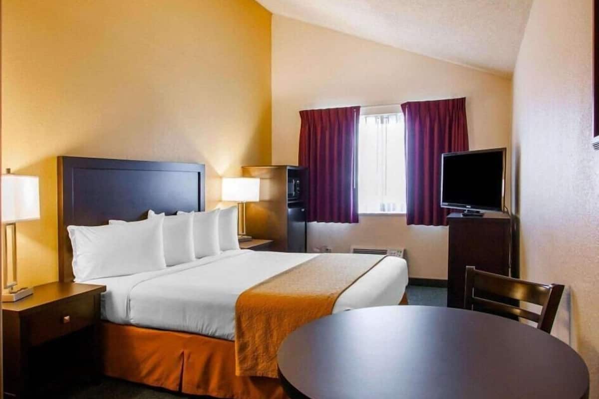 A hotel room with a bed, bedside tables, a TV, a desk, and a chair.