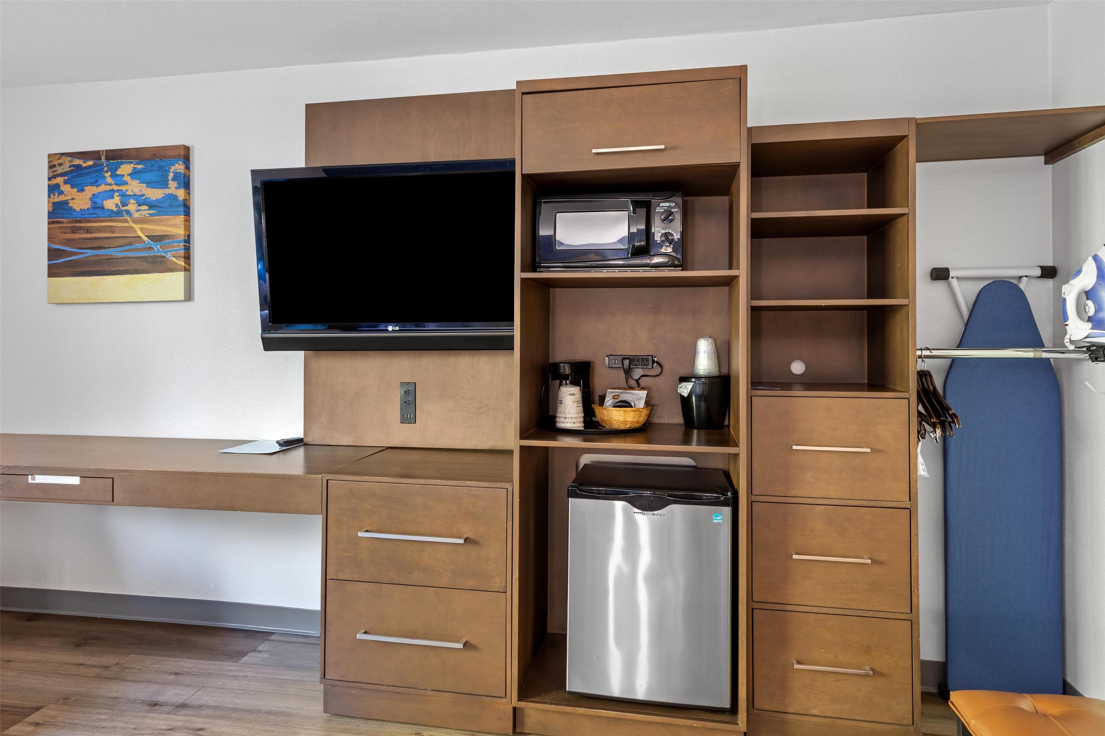 A compact kitchenette with a microwave, refrigerator, and a flat-screen TV mounted on the wall.