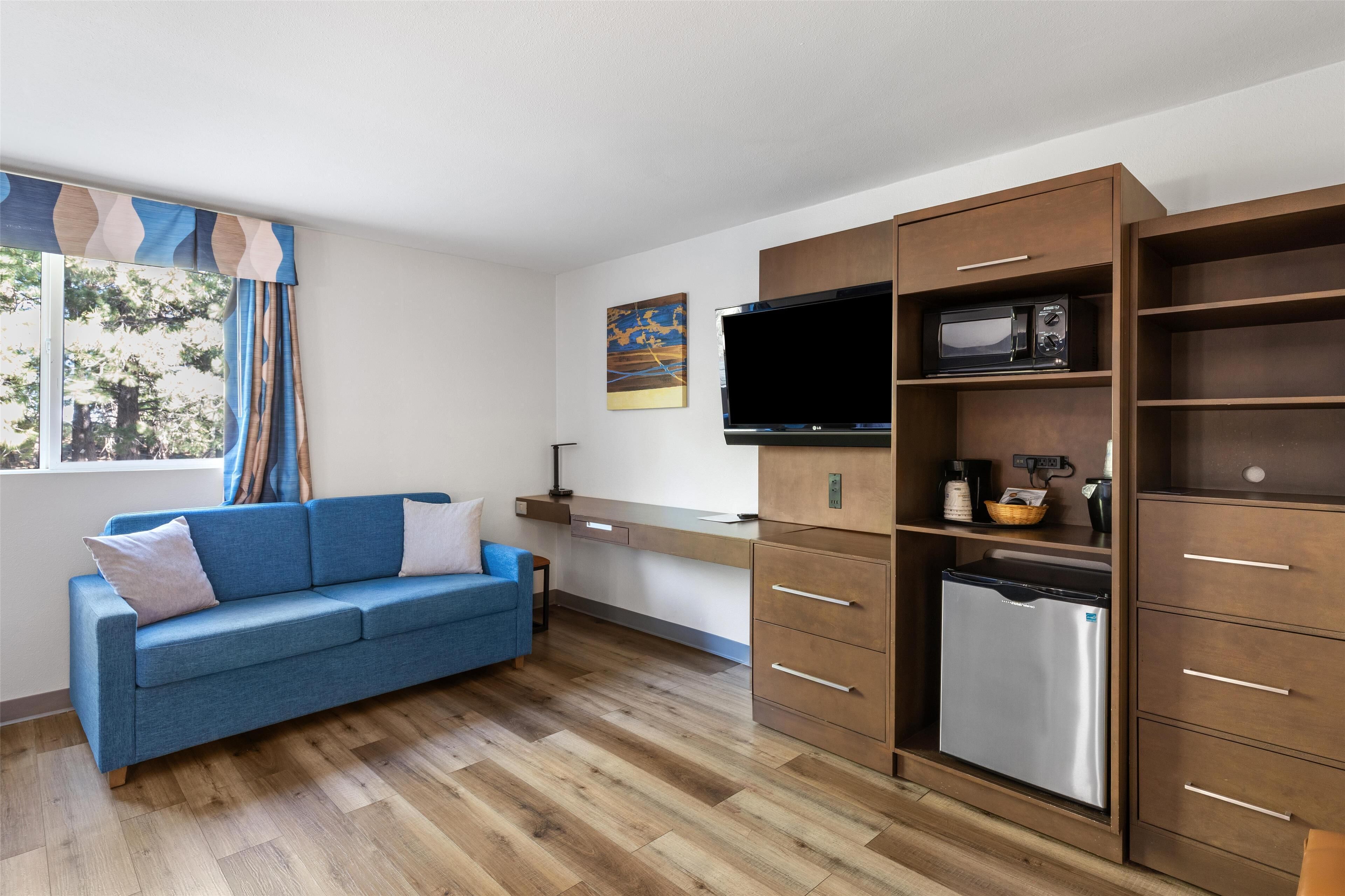 Un espace de vie compact comprenant un canapé bleu, des meubles en bois, un four à micro-ondes encastré et un téléviseur à écran plat.