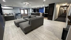 Ein modernes Wohnzimmer mit Ecksofa und Hocker, einem Küchenbereich und einem Flur, der zum Schlafzimmer führt.