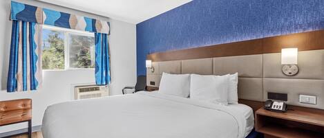 A modern hotel room with a large bed, a wooden nightstand, a desk, and a window with blue curtains.