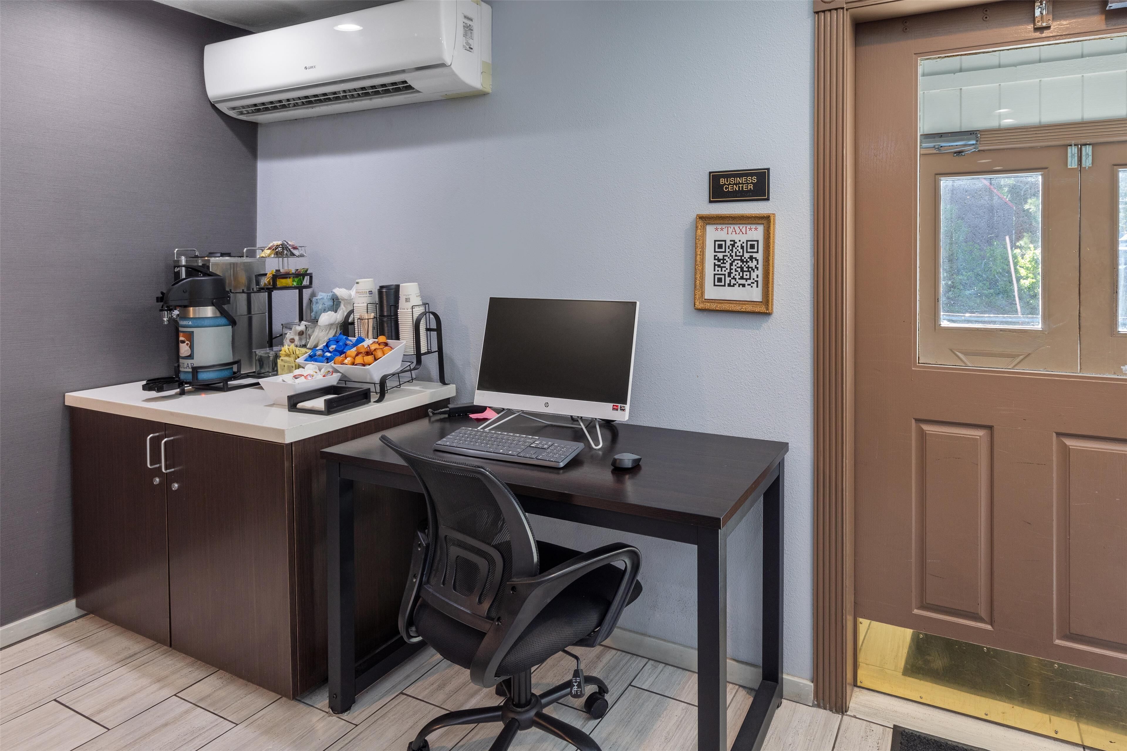 Un espacio de oficina moderno con un escritorio, computadora y material de oficina. Hay una puerta marrón con ventana y un letrero que dice "BUSINESS CENTER".