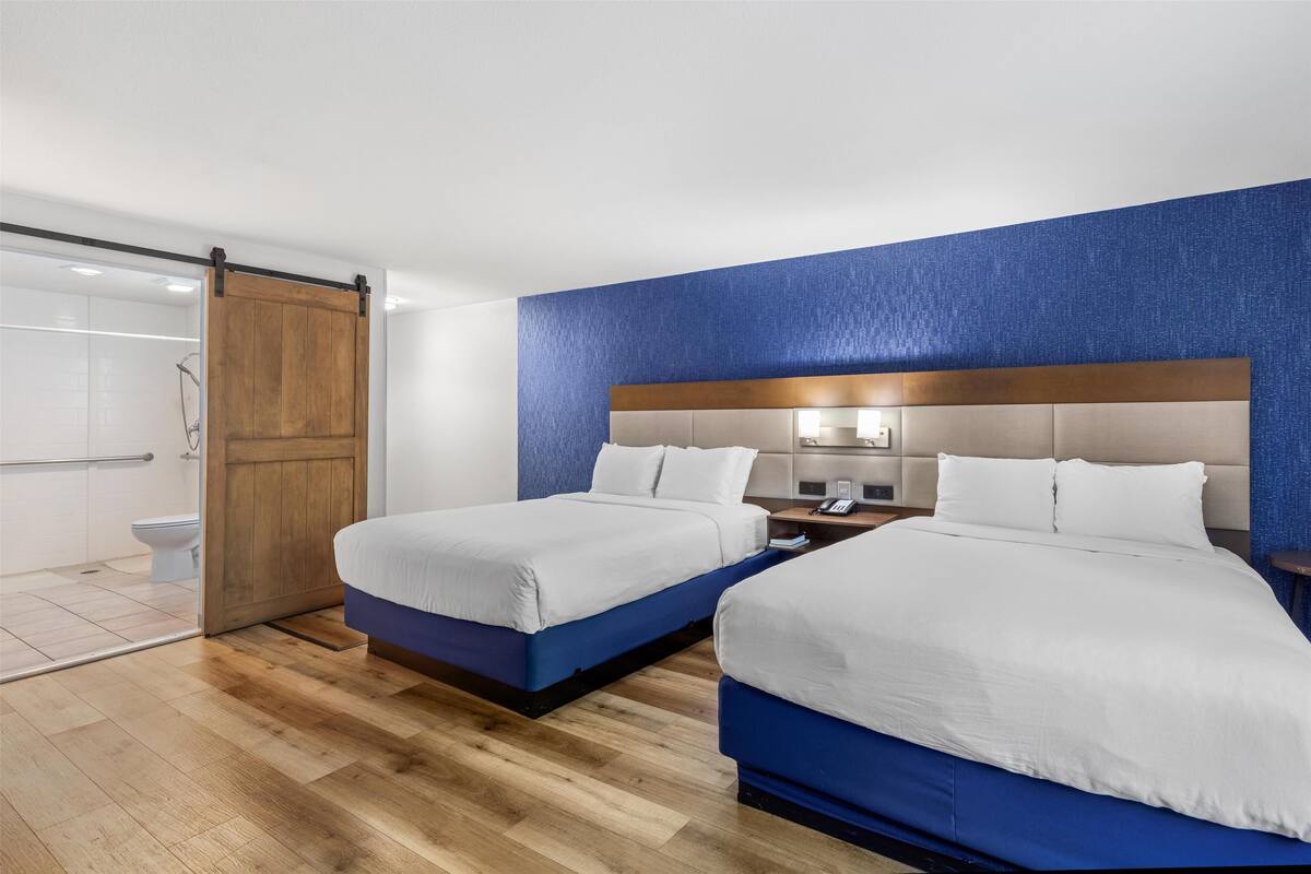 Habitación de hotel con dos camas, una puerta de madera, zona de ducha y una pared azul decorativa.