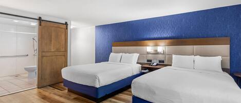 Quarto de hotel com duas camas, porta de madeira, área de chuveiro e parede com detalhes em azul.