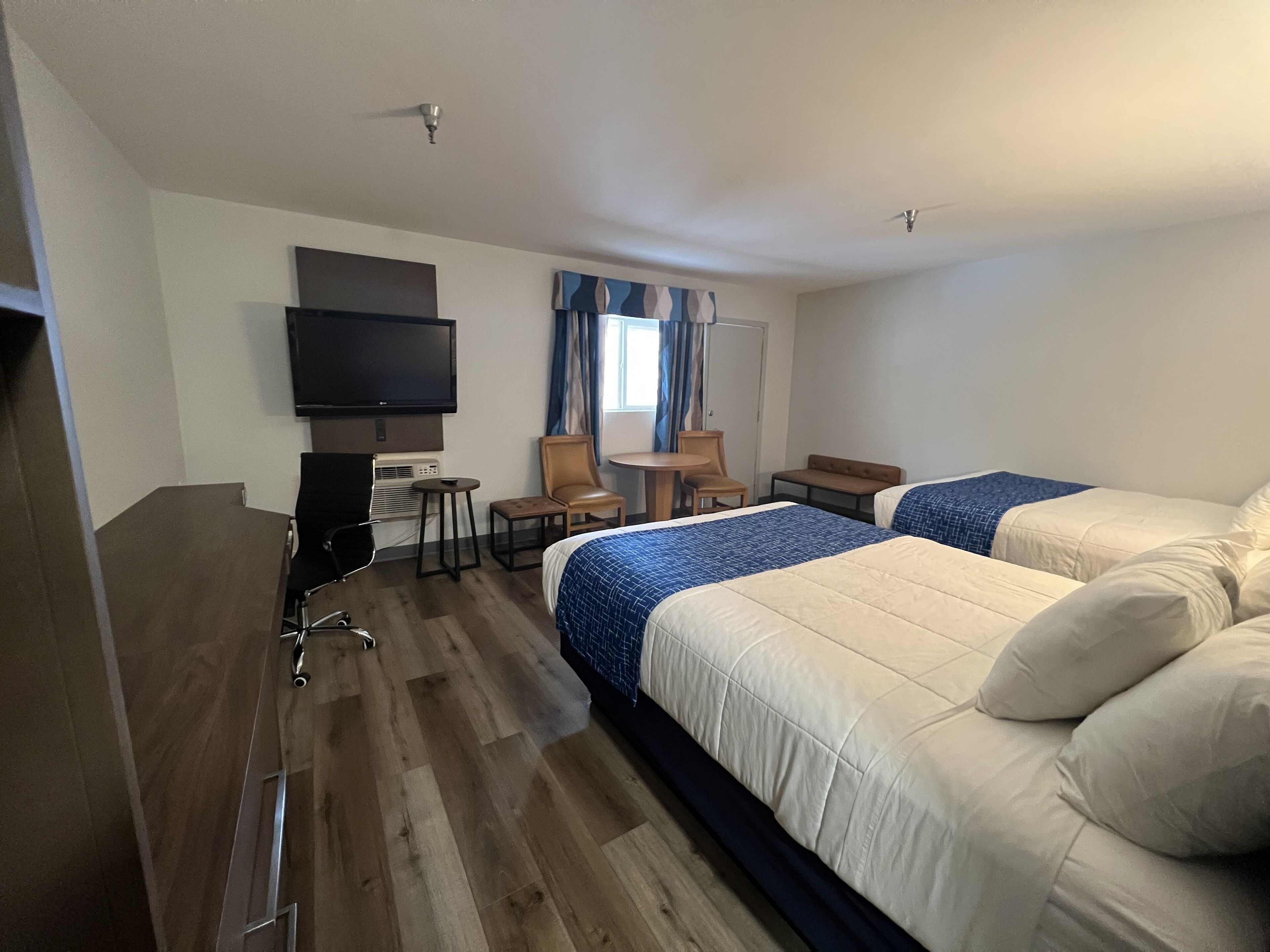Habitación de hotel con dos camas, televisión, escritorio con silla y ventana con cortinas.
