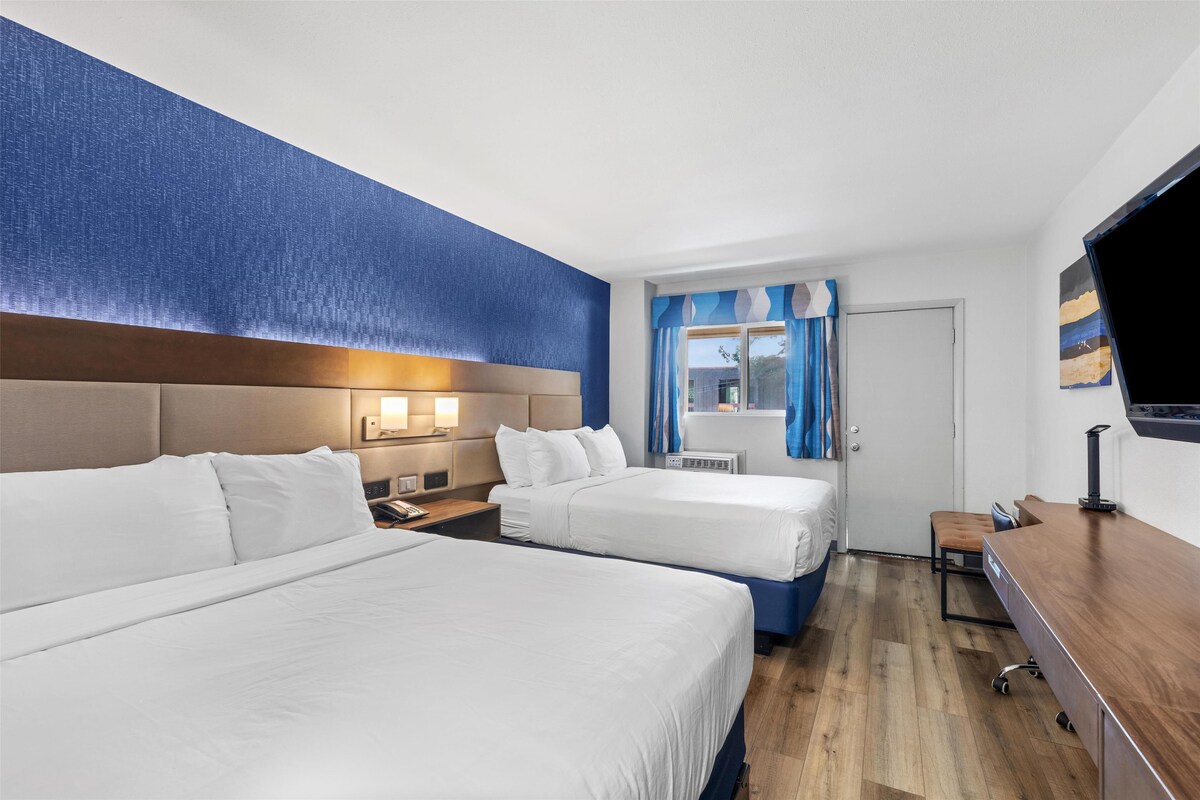 Une chambre d’hôtel avec deux lits, un bureau, une télévision et une fenêtre avec des rideaux.