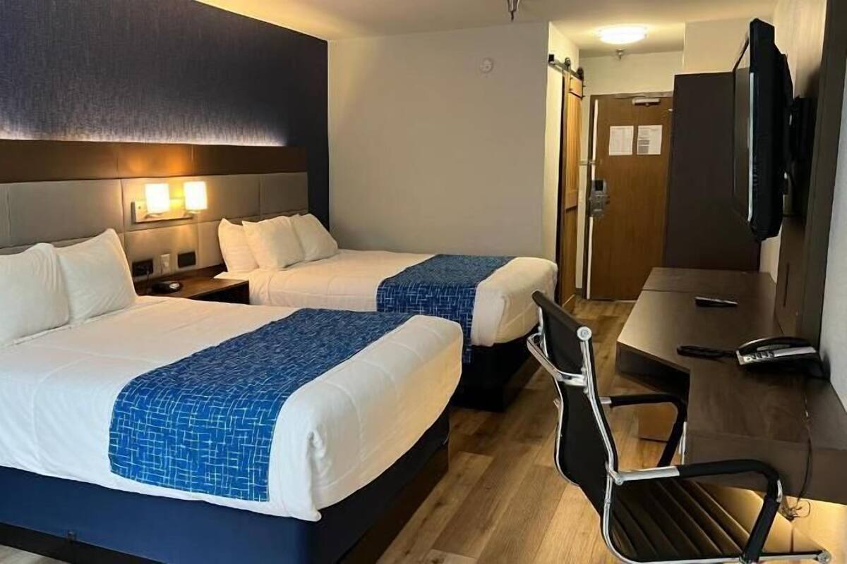 Habitación de hotel con dos camas, un escritorio, una silla y un televisor.