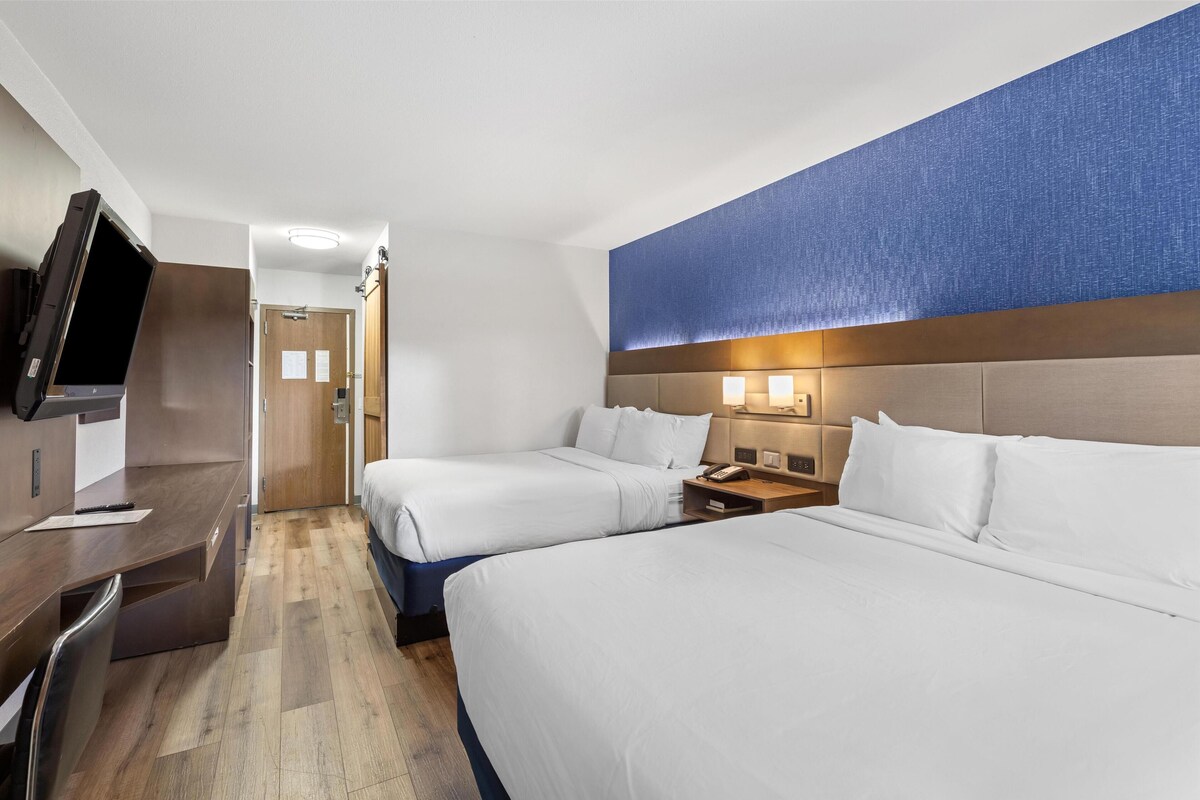 Une chambre d’hôtel avec deux lits, un bureau, une télévision et une porte de salle de bain.