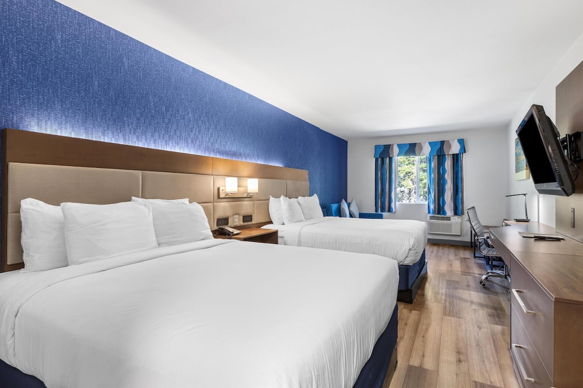 Habitación de hotel con dos camas, un escritorio, un televisor y una ventana con cortinas.
