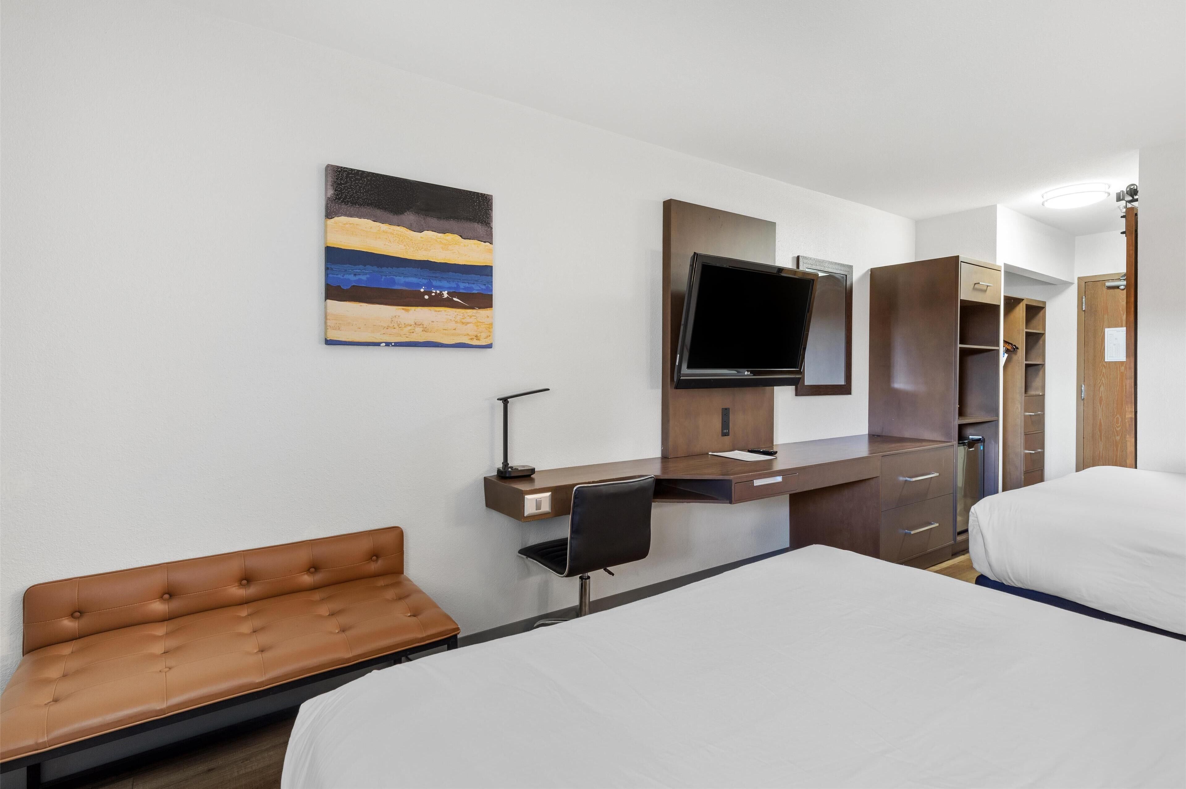 A hotel room with a bed, a desk with a chair, a TV, and a wardrobe.
