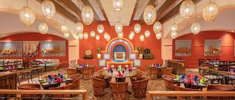 A restaurant with round tables, wicker chairs, and hanging wicker lamps.