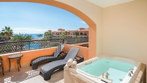 Un balcón con vistas al mar, un jacuzzi y sillones de descanso.