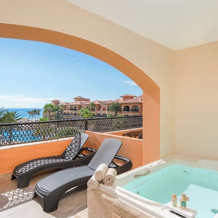 A balcony with a view of the sea, a jacuzzi, and lounge chairs.