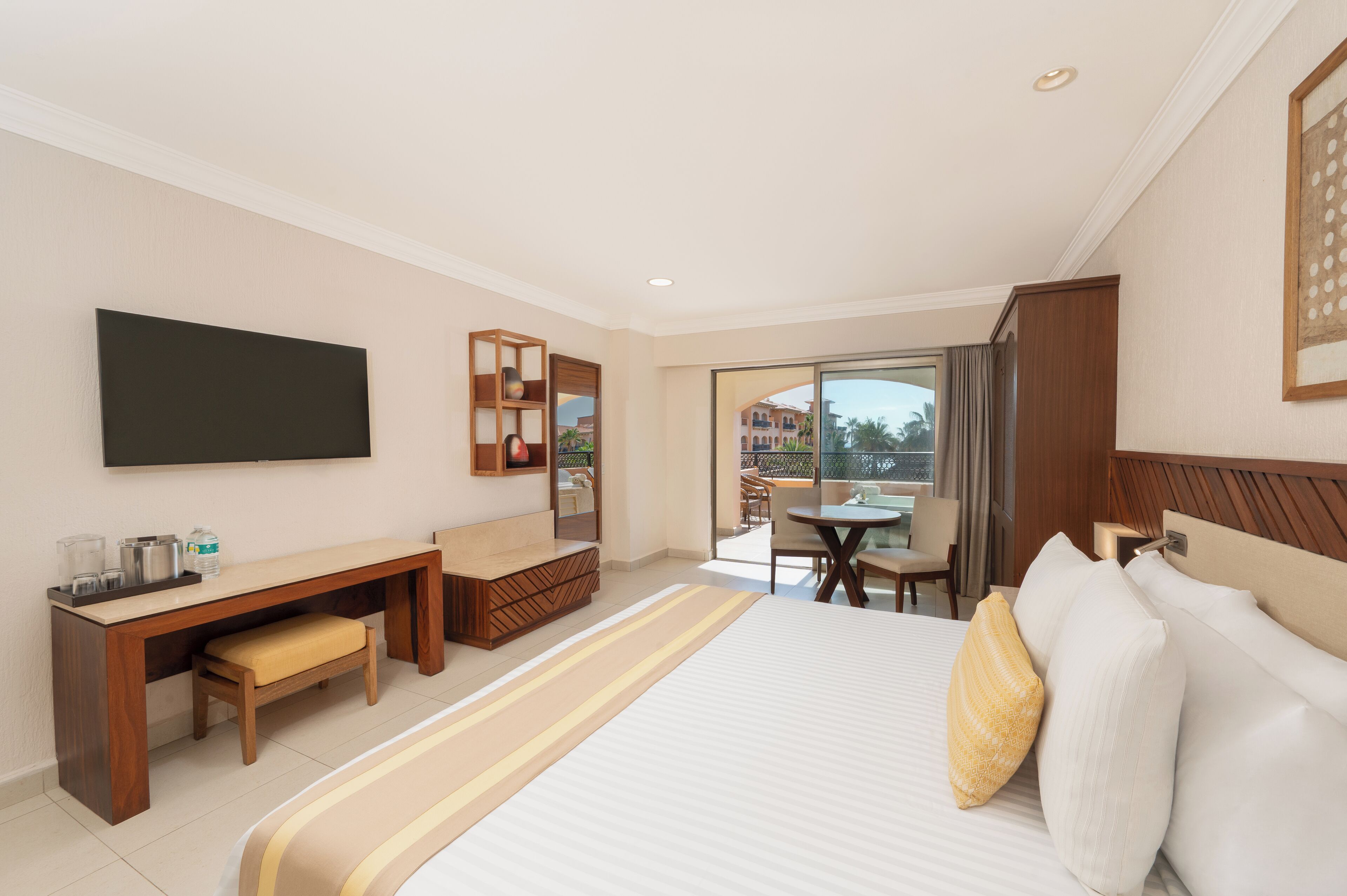 A hotel room with a large bed, a desk with a chair, a television, and a balcony with a table and chairs.