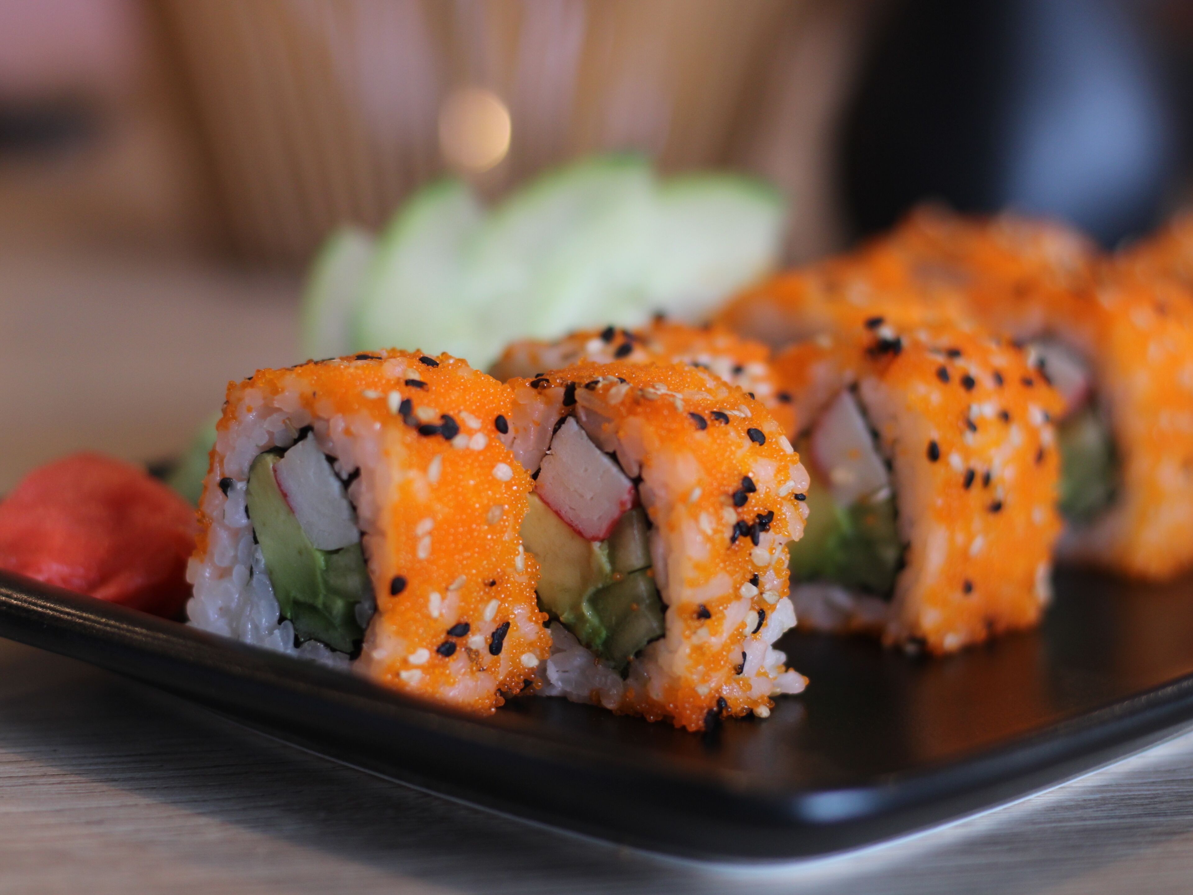 Sushi rolls with sesame seeds on a black plate.