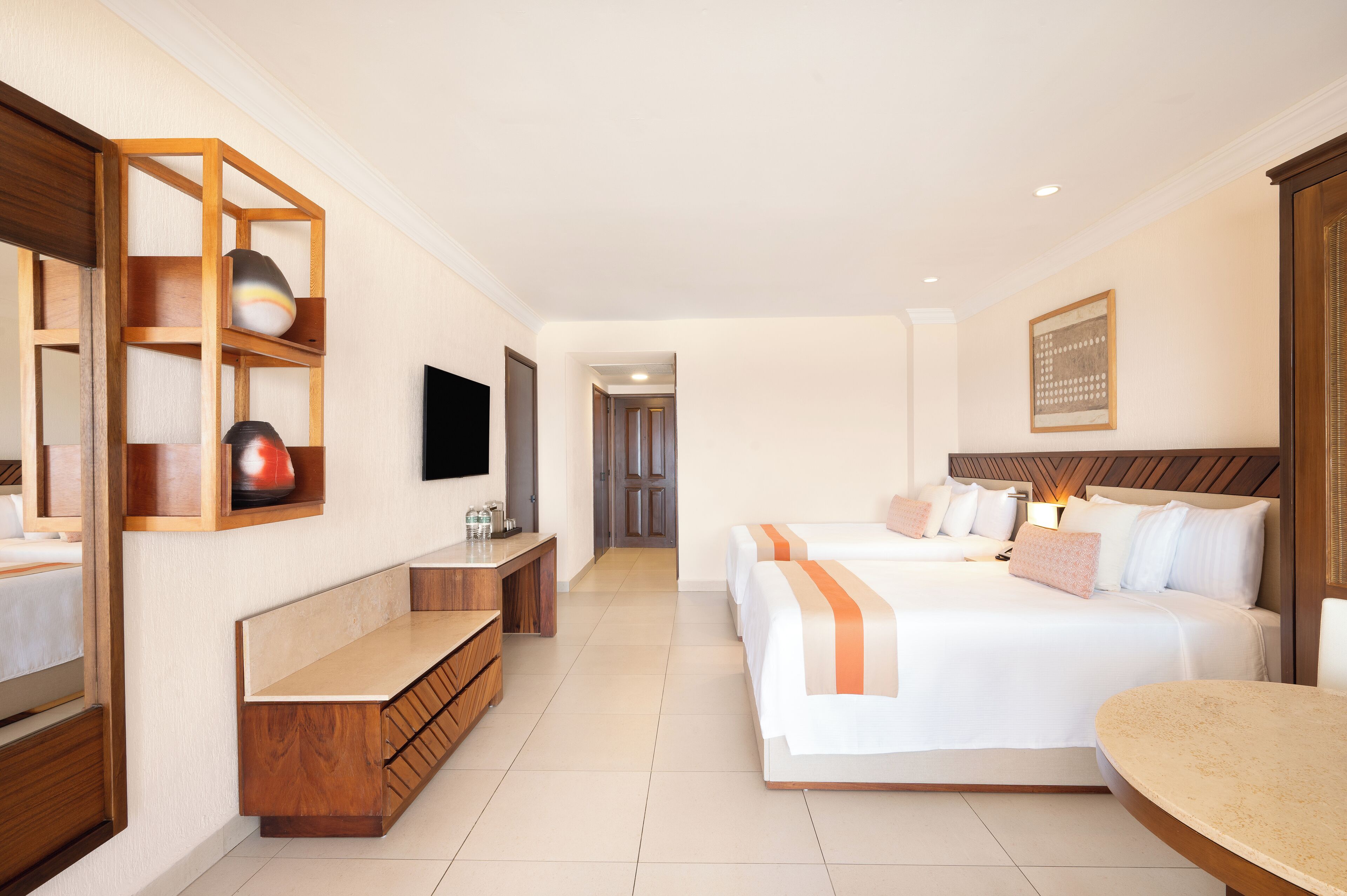 Une chambre d’hôtel avec un grand lit, un bureau, une télévision et une étagère en bois ornée d’objets décoratifs.