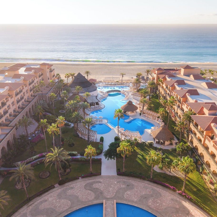 A resort with multiple swimming pools, a beach view, and a courtyard with palm trees.