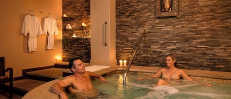 A spa with a hot tub, stone walls, and a Buddha statue.