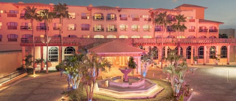 A hotel with a courtyard, palm trees, and a fountain.