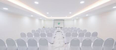 Ein Konferenzraum mit Reihen weißer Stühle, einer Projektionsleinwand vorne und einem Marmorboden.