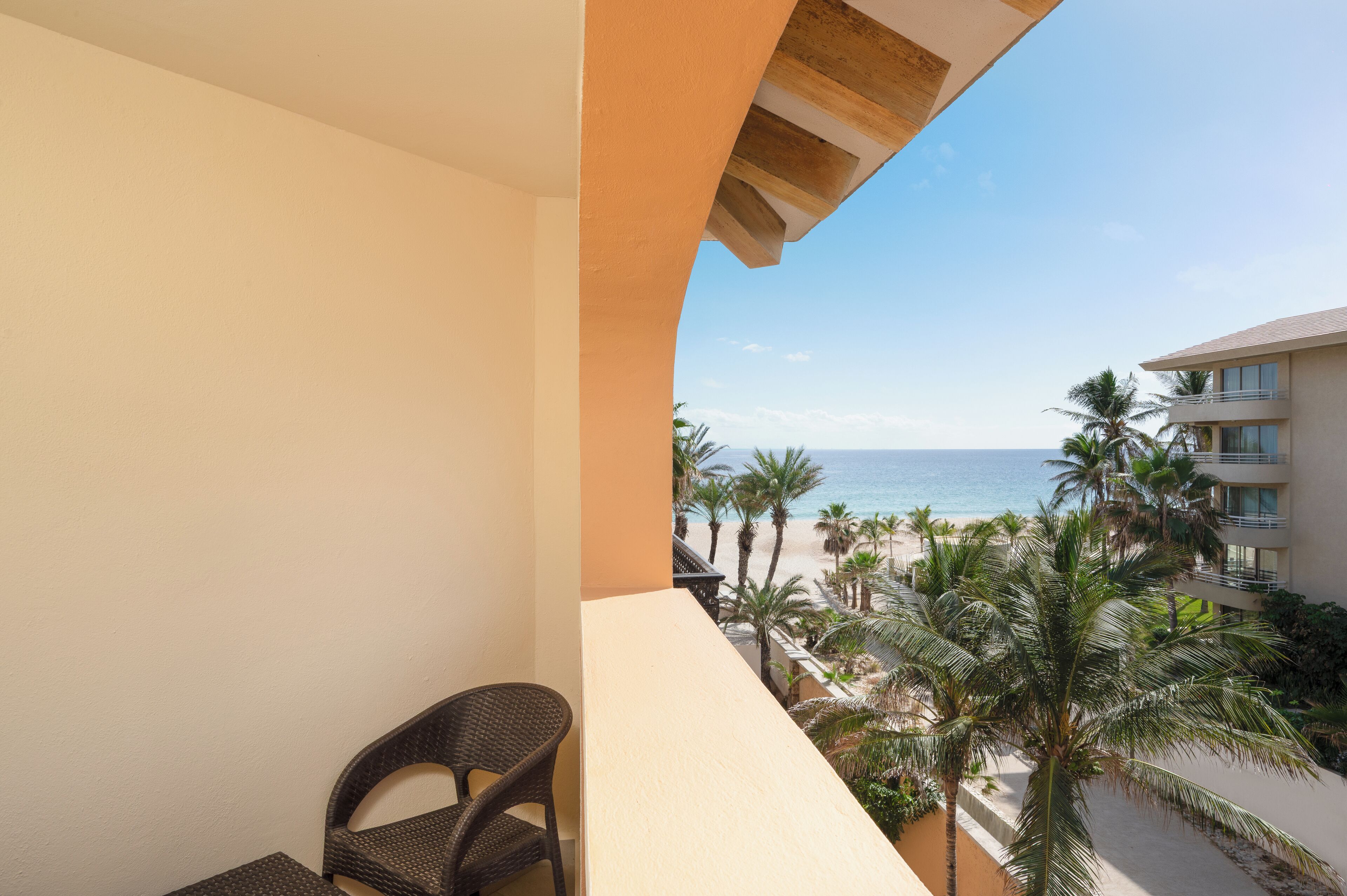 A balcony with a view of the beach and palm trees.