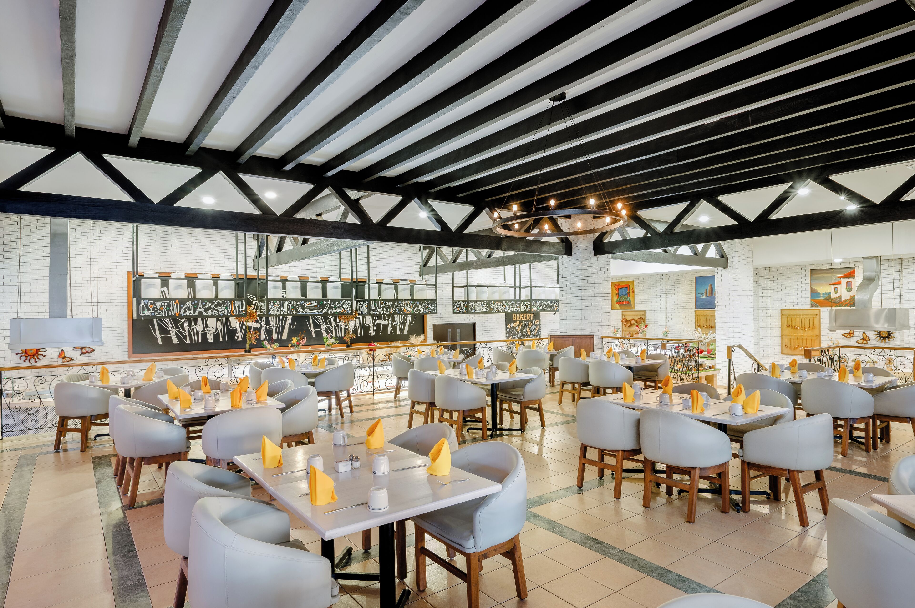 Een restaurant met een modern interieur, met een hoge plafond met zichtbare balken, een centrale kroonluchter en verschillende zithoekopstellingen, waaronder tafels en stoelen.