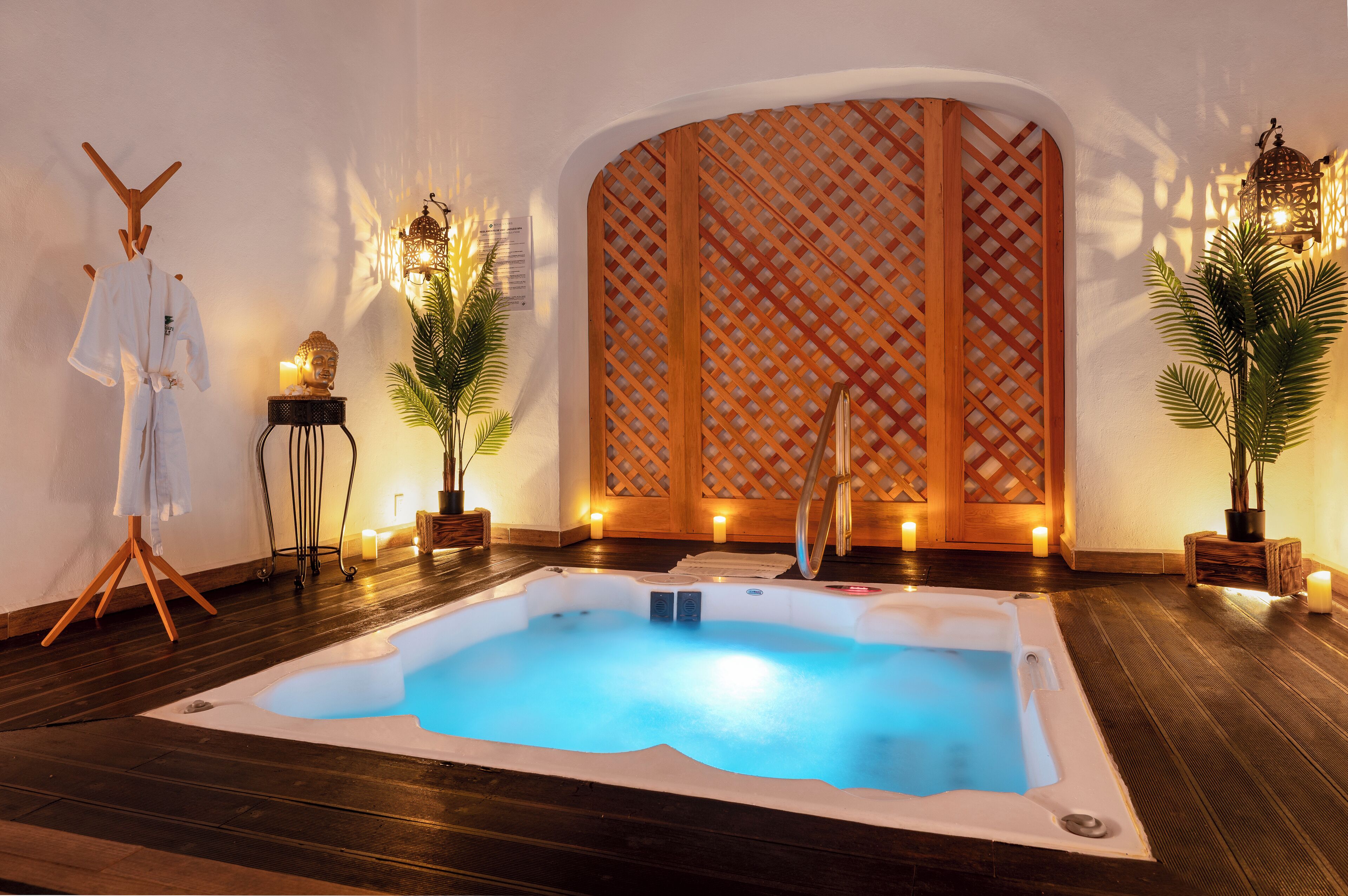 A spa area with a hot tub, wooden floor, a Buddha statue, and a wooden lattice partition.