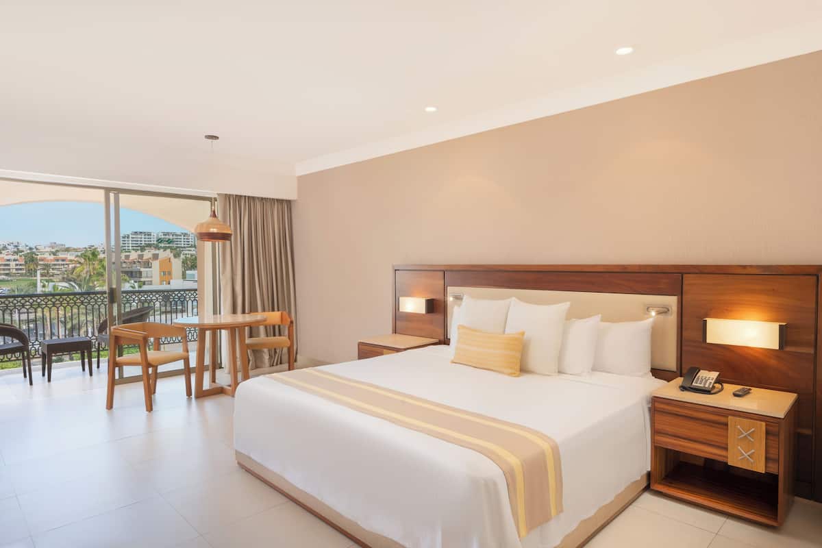 Een hotelkamer met een groot bed, een bureau, een stoel, een balkon met uitzicht op de stad en een nachtkastje met een telefoon.