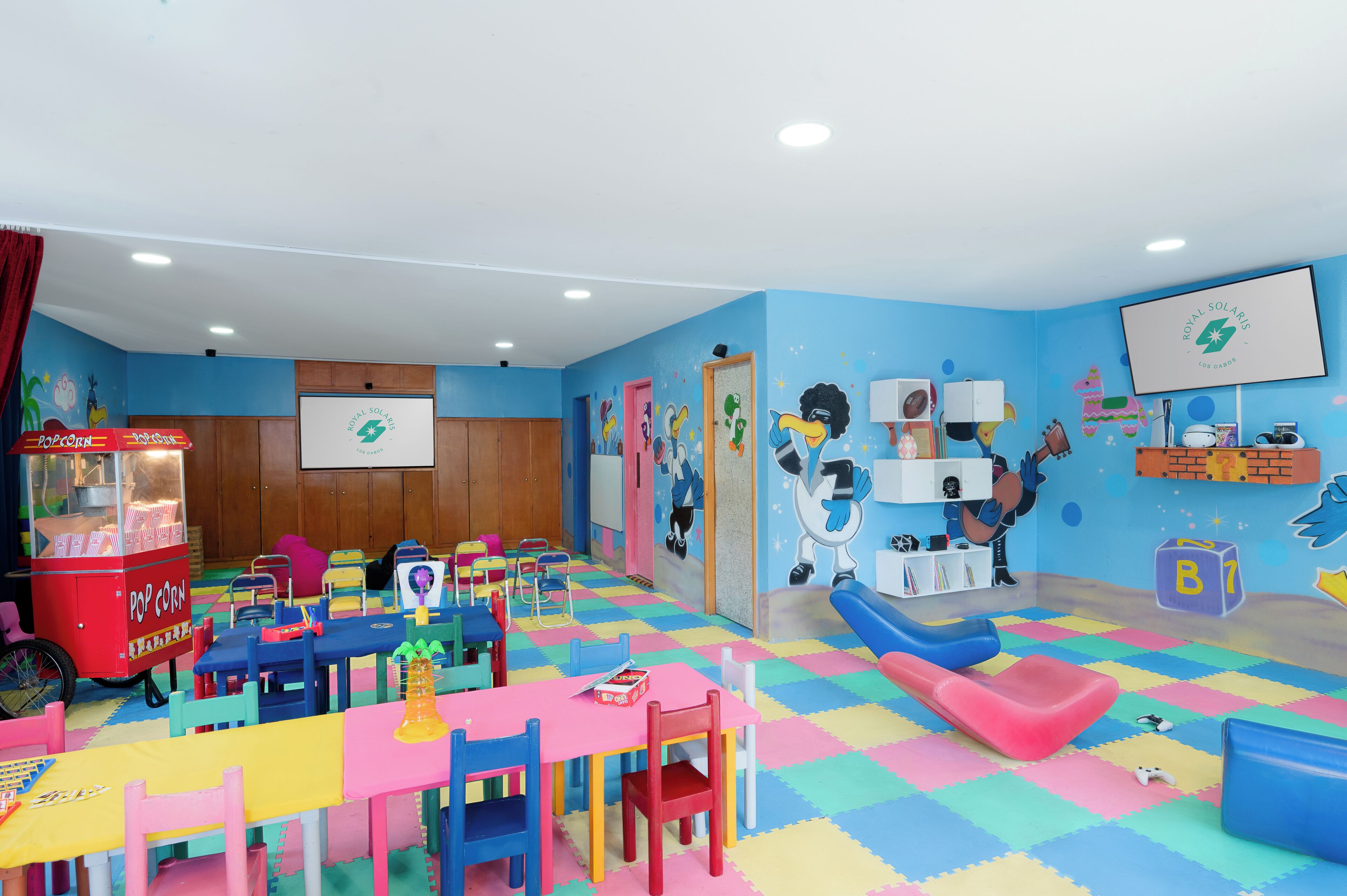 Une salle de jeux pour enfants avec des meubles aux couleurs vives, un chariot à pop-corn et des décorations murales ludiques.