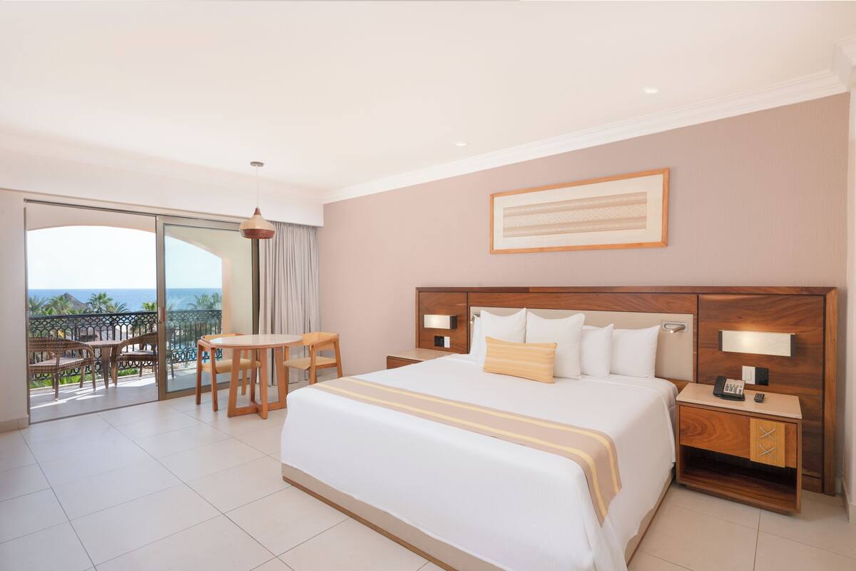 Een hotelkamer met een groot bed, een bureau en een stoel. Er is een balkon met uitzicht op de oceaan.
