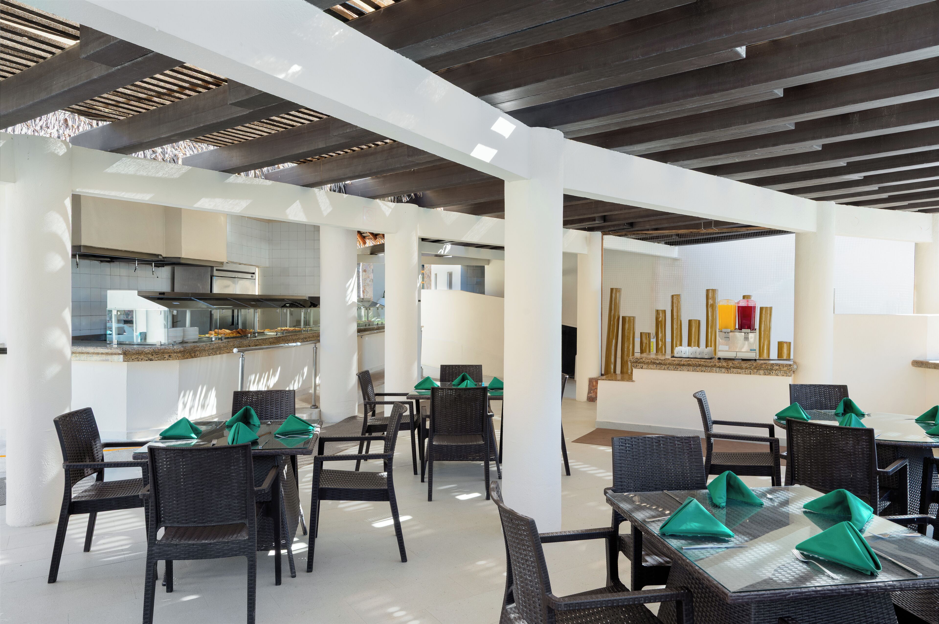 A modern dining area with wicker chairs and tables, a kitchen in the background, and a bar area.