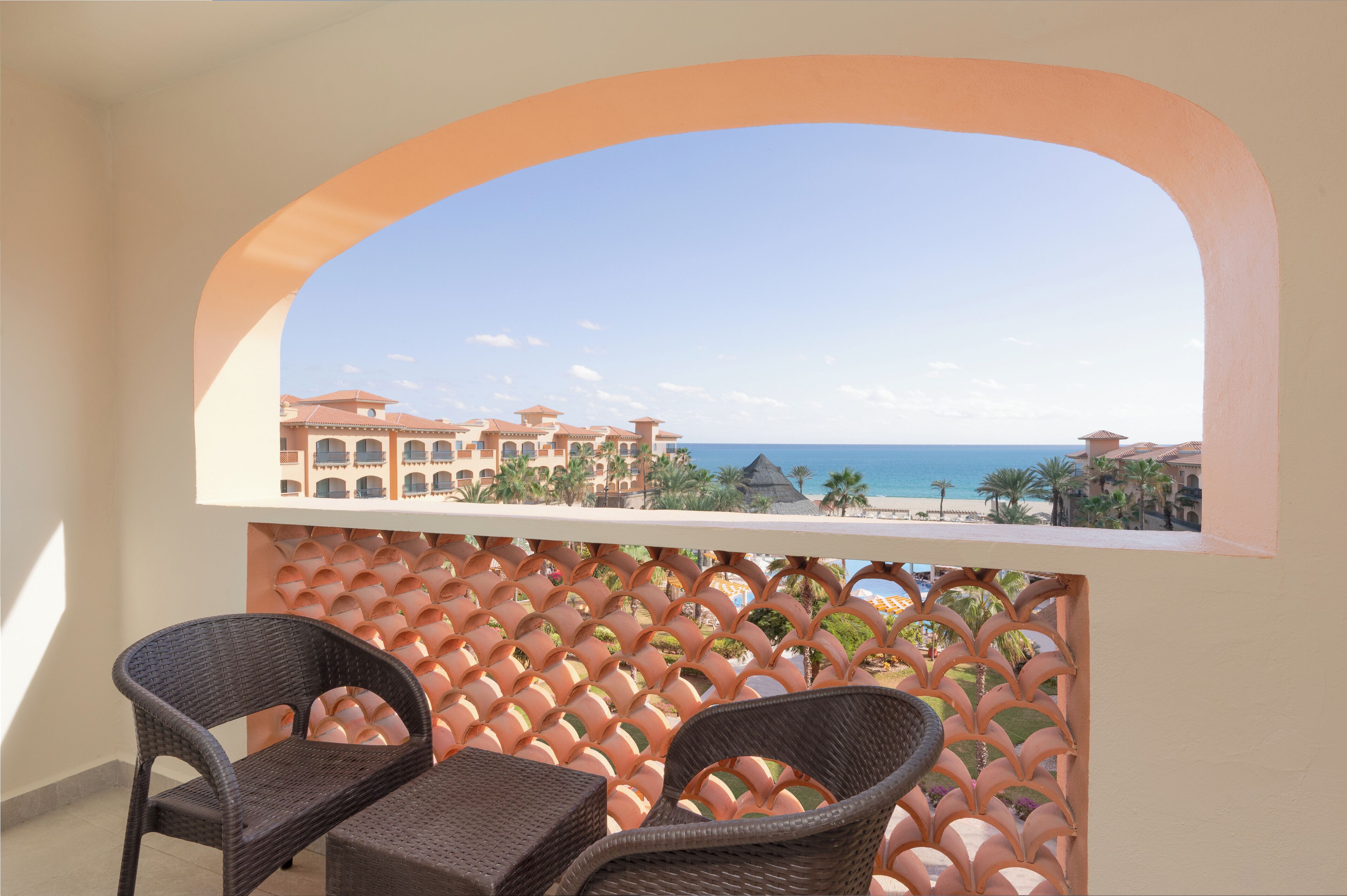 Un balcon avec des fauteuils en osier et une vue sur un complexe hôtelier en bord de mer.