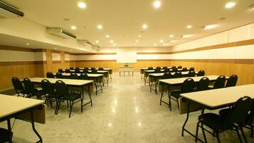 Uma sala de conferências com várias mesas e cadeiras, unidades de ar condicionado e um quadro branco.