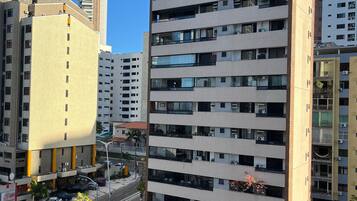 A high-rise building with multiple balconies, a parking area, and a clear sky.