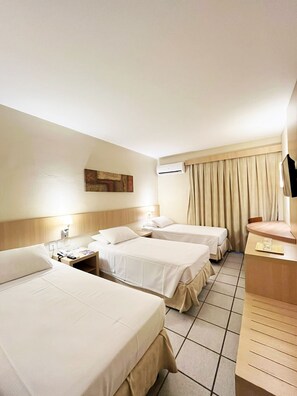 Habitación de hotel con tres camas, un escritorio, una silla, un televisor y un equipo de aire acondicionado.