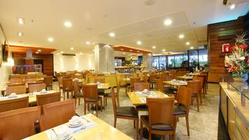 Un ampli restaurant amb diverses taules i caires, una zona de bar central i grans finestrals que ofereixen vistes a l'exterior.