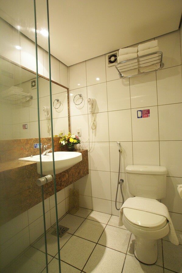 Une salle de bain dotée d’une douche à parois de verre, d’un lavabo avec un plan de toilette en marbre, de toilettes et d’un porte-serviettes avec des serviettes.