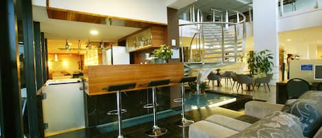A modern hotel lobby with a bar area, seating, a staircase, and a pool.